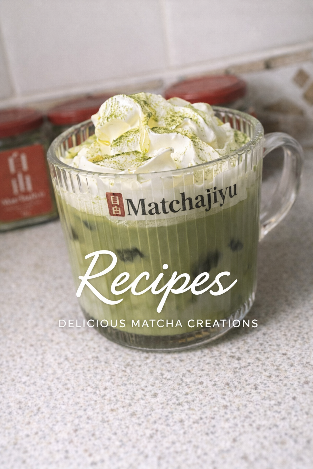 Matcha latte with whipped cream in a clear mug on a countertop, featuring Matchajiyu branding. Iced Blueberry matcha latte